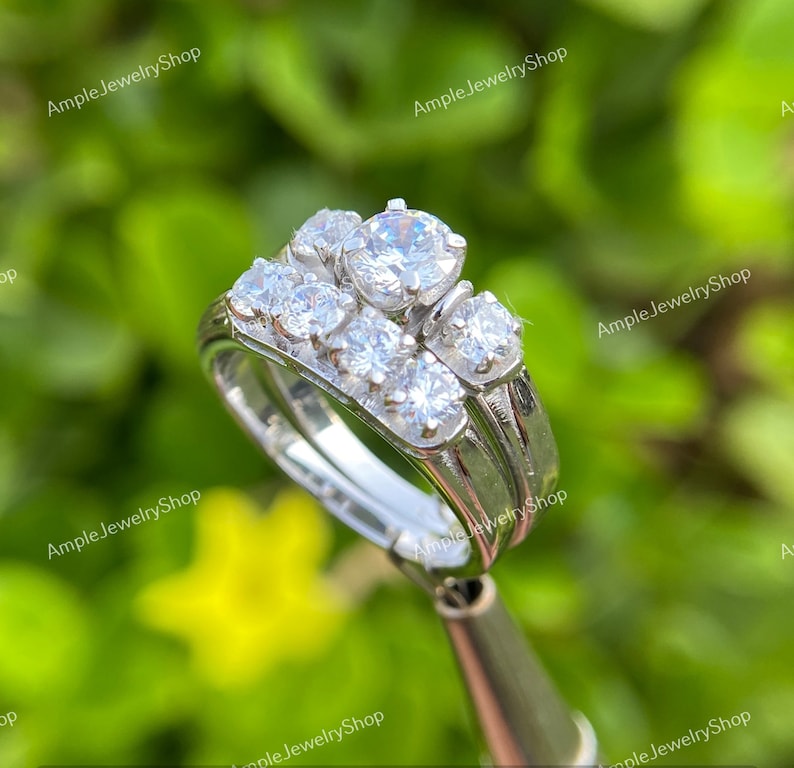 May include: A silver wedding band set with a cluster of five round-cut diamonds. The center diamond is larger than the surrounding diamonds.