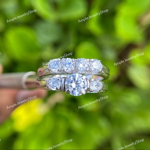 May include: A set of two silver engagement rings with a large round diamond in the center of the bottom ring and a row of smaller diamonds in the top ring.