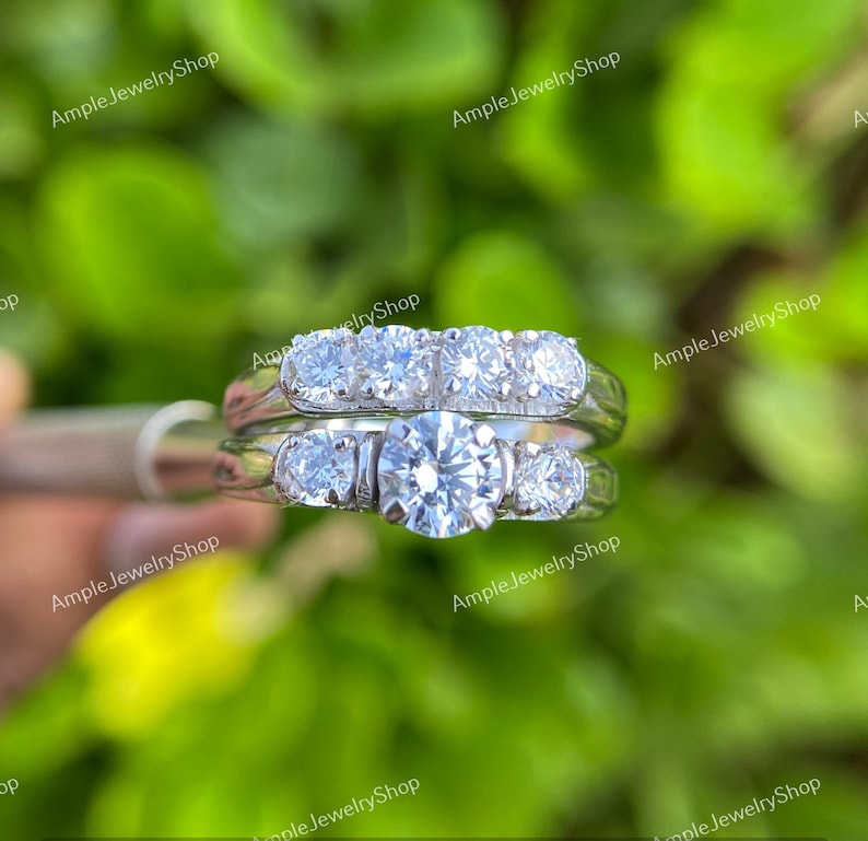 May include: A set of two silver engagement rings with a large round diamond in the center of the bottom ring and a row of smaller diamonds in the top ring.