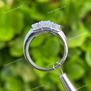 May include: A silver ring with three round diamonds set in a prong setting. The ring is shown from the side, with the diamonds facing the camera.