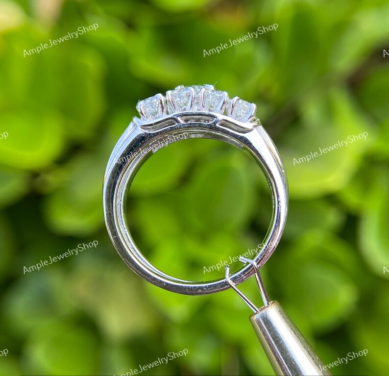 May include: A silver ring with three round diamonds set in a prong setting. The ring is shown from the side, with the diamonds facing the camera.