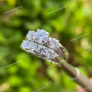 May include: A silver wedding band set with a large round center stone and smaller stones on the band. The band is set with a row of smaller stones.