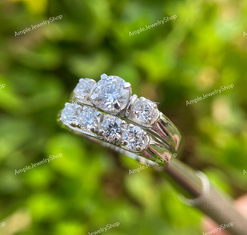 May include: A silver wedding band set with a large round center stone and smaller stones on the band. The band is set with a row of smaller stones.