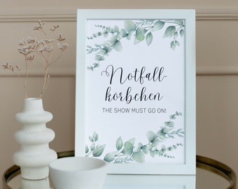 May include: White framed print with green watercolor leaves and the text "Notfall-körbchen THE SHOW MUST GO ON!"