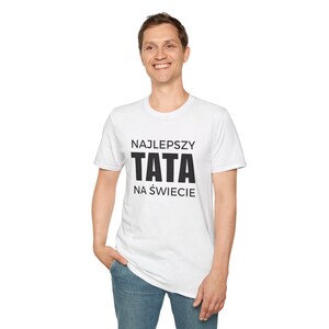 May include: White t-shirt with the text "NAJLEPSZY TATA NA ŚWIECIE" in black, meaning "Best Dad in the World" in Polish. The shirt is worn by a person in blue jeans.
