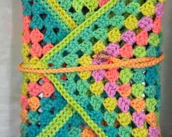 May include: A crocheted pouch with a granny square pattern in shades of green, pink, orange, and yellow. The pouch is folded over and secured with a button.