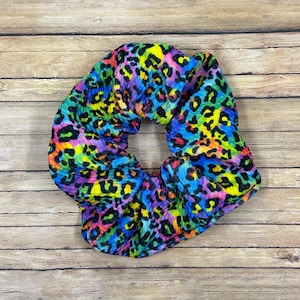 May include: A colorful leopard print scrunchie with a rainbow pattern. The scrunchie is made of a soft, stretchy fabric and is perfect for holding hair in place.