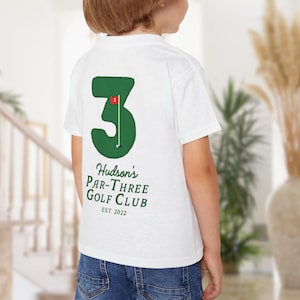 May include: White t-shirt with a green number 3 and a golf flag graphic. The text "Hudson's Par-Three Golf Club EST. 2022" is printed below the graphic. The shirt is worn by a person.