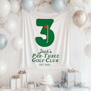 May include: A white banner with a large green number 3, a golf flag, and the text "Jack's Par-Three Golf Club EST. 2022". The banner is surrounded by white, silver, and gold balloons, gifts, and a cake.