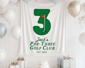 May include: A white banner featuring a green number 3, a golf flag, and the text "Jack's Par-Three Golf Club EST. 2022". The scene includes white, silver, and gold balloons, gifts, and a cake, creating a celebratory atmosphere.
