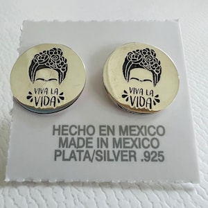 Puede incluir: Un par de pendientes de plata con una imagen en blanco y negro de Frida Kahlo y el texto "Viva la Vida". Los pendientes están hechos en México y son de plata .925.