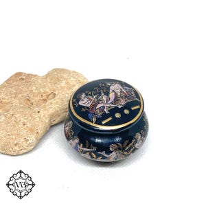 Può includere: Una piccola scatola rotonda in ceramica nera con un bordo dorato e una scena dipinta a colori di figure greche sul coperchio.