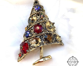 May include: A gold-tone Christmas tree brooch with red, blue, and clear rhinestones. The tree is decorated with a gold filigree design.