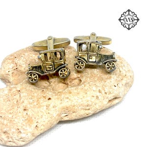 Op de afbeelding: Een paar gouden manchetknopen met een vintage auto-ontwerp. De auto's zijn versierd met zwarte accenten en hebben een licht verhoogd ontwerp.