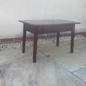 May include: A small, square wooden table with a dark brown finish. The table has four straight legs and a simple design. It is approximately 60 cm wide and 60 cm long.