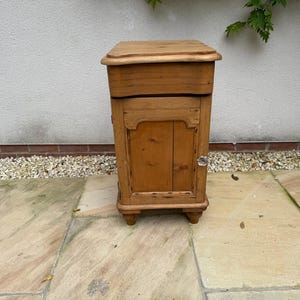 May include: A small, antique wooden cabinet in a light brown colour. The cabinet has a rectangular shape with a hinged door and a small, rounded top. It stands on four small, rounded feet. The cabinet is likely used for storage.
