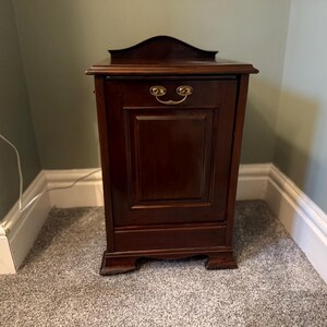 May include: A dark brown wooden cabinet with a curved top and brass hardware. The cabinet has a rectangular door with a recessed panel and sits on a carpeted floor. The cabinet is approximately 76 cm tall.