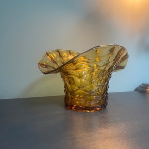 May include: A vintage amber glass vase with a ruffled top and a textured diamond pattern. The vase is sitting on a grey surface.