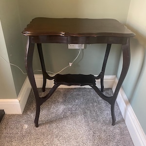 May include: A dark brown wooden side table with a scalloped top and a lower shelf. The table has four legs with a curved design.