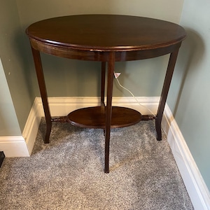 May include: A dark brown oval-shaped side table with a lower shelf. The table has three legs and is made of wood.