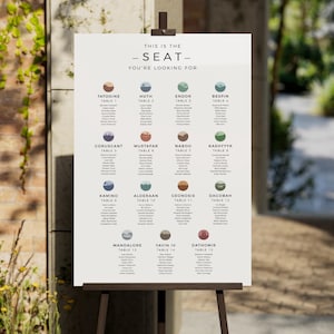 May include: A white wedding seating chart sign on a wooden easel featuring the text THIS IS THE SEAT YOU'RE LOOKING FOR. The chart displays fifteen tables named after fictional planets, each with a circular icon and a list of guest names.