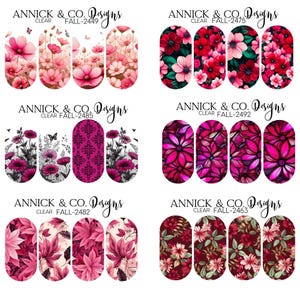 Peut inclure: Plusieurs modèles de nail art transparents avec des motifs floraux dans des tons de rose, de rouge et de bordeaux. Les motifs comprennent divers types de fleurs et de feuilles, certains avec des papillons. La marque "ANNICK & CO. Designs" est visible.