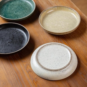Puede incluir: Cuatro platos de cerámica en tonos verdes, negros y crema, con texturas moteadas. Los platos están dispuestos sobre una superficie de madera, mostrando sus diferentes colores y acabados. Los platos tienen un diseño simple y moderno.