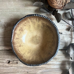 May include: A rustic, brown ceramic bowl with a black rim and a textured, uneven surface. The bowl is empty and sits on a wooden surface.