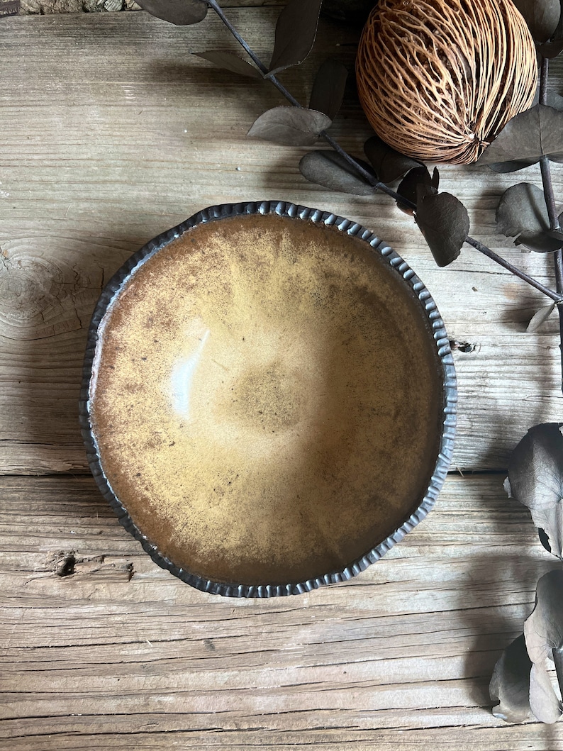 May include: A rustic, brown ceramic bowl with a black rim and a textured, uneven surface. The bowl is empty and sits on a wooden surface.