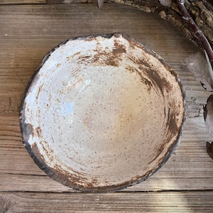 Puede incluir: Un cuenco de cer&aacute;mica blanca con un borde marr&oacute;n y un esmalte moteado. El cuenco est&aacute; sobre una superficie de madera.