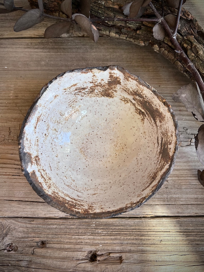 Puede incluir: Un cuenco de cer&aacute;mica blanca con un borde marr&oacute;n y un esmalte moteado. El cuenco est&aacute; sobre una superficie de madera.