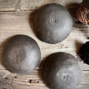 May include: Three dark gray ceramic bowls with a slightly textured surface. The bowls are round and have a slight lip around the edge.