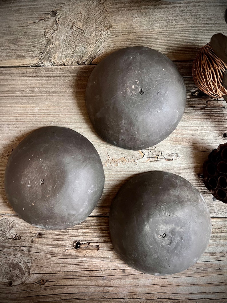 May include: Three dark gray ceramic bowls with a slightly textured surface. The bowls are round and have a slight lip around the edge.