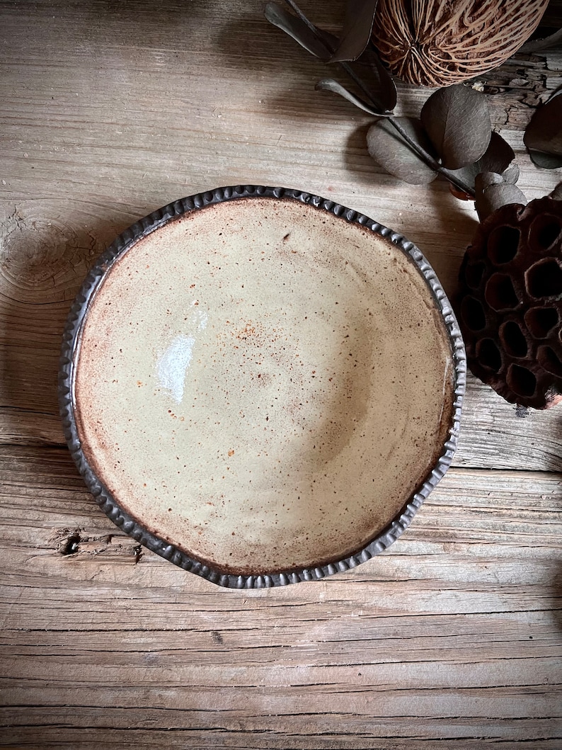 May include: A white ceramic bowl with a brown rim and a speckled glaze. The bowl is sitting on a wooden surface.