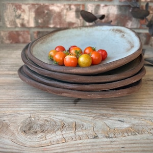 May include: A stack of four ceramic plates with a light blue glaze. The top plate has a small pile of red and yellow tomatoes in the center.