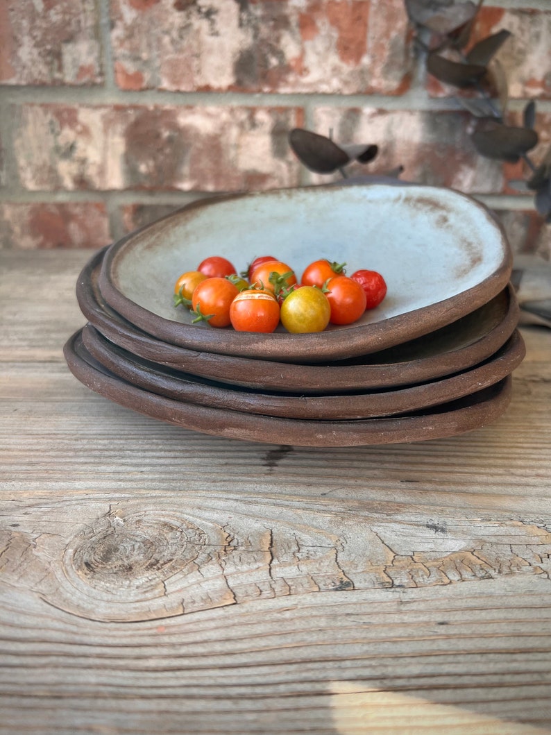 May include: A stack of four ceramic plates with a light blue glaze. The top plate has a small pile of red and yellow tomatoes in the center.