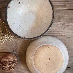 May include: Two ceramic bowls with speckled white glaze and a dark brown rim. The larger bowl is sitting on top of the smaller bowl.