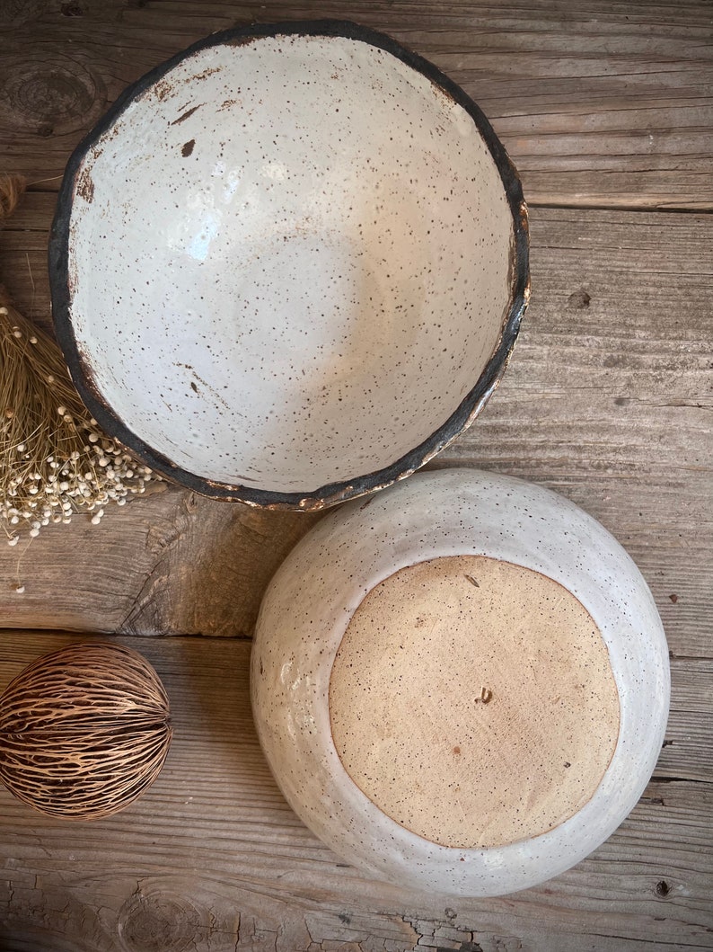 May include: Two ceramic bowls with speckled white glaze and a dark brown rim. The larger bowl is sitting on top of the smaller bowl.
