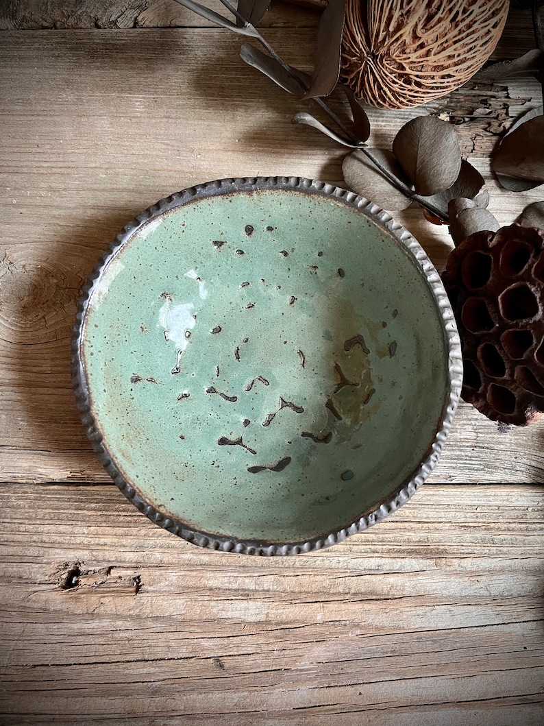 May include: A green ceramic bowl with a textured rim. The bowl has a speckled glaze and a dark brown rim.