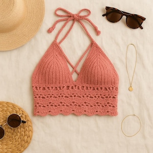 May include: A coral-colored, handmade crochet halter top with a crisscross design. The top features a scalloped edge and is displayed with sunglasses, a necklace, and a straw hat, suggesting a summer theme.