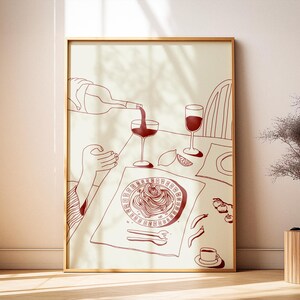 Puede incluir: Ilustración enmarcada de una escena de comedor, que muestra una botella vertiendo vino en una copa. También se ven un plato de pasta, una segunda copa de vino y una taza de café. La obra de arte es en tonos rojos y beige.