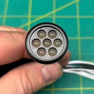 May include: Close-up of a black connector with nine round, clear LED lights. The connector is attached to a bundle of wires, including red, black, and white wires.