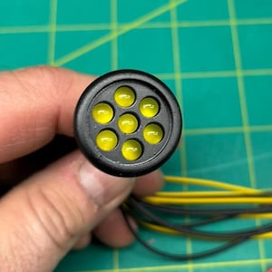 Puede incluir: Una luz LED negra y amarilla con 10 pequeñas luces LED amarillas. La luz está conectada a un conjunto de cables con diferentes colores.