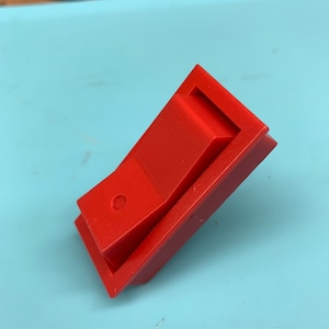 Puede incluir: Un interruptor de palanca de plástico rojo con un botón redondo.
