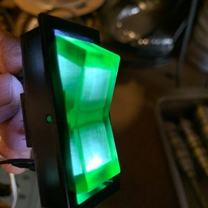 May include: A green illuminated toggle switch with a black plastic housing.
