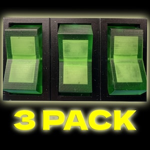 Puede incluir: Tres interruptores de palanca negros con palancas translúcidas verdes. Los interruptores vienen en un paquete de 3. El texto "3 PACK" está impreso en amarillo debajo de los interruptores.