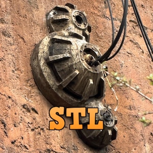 Puede incluir: Primer plano de un objeto metálico desgastado con forma circular y superficie texturizada. El objeto está fijado a una pared de ladrillo y tiene varios cables conectados a él. El texto "STL" es visible en la parte inferior de la imagen.