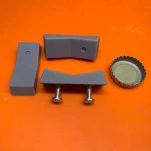 May include: Three gray plastic pieces with a hole in the center, two screws, and a silver bottle cap.