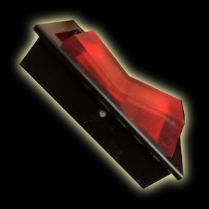 Puede incluir: Un interruptor basculante rojo con una carcasa de plástico negro. El interruptor está en posición de apagado.