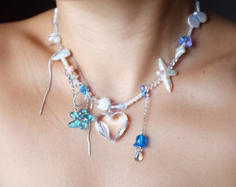 May include: A delicate necklace with a crystal heart pendant, blue and white beads, and a starfish charm. The necklace is made with a variety of materials, including pearls, shells, and glass beads.